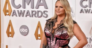 Miranda Lambert wears a pink-and-black lace dress in front of a CMA Awards backdrop