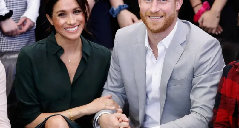 Meghan Markle and Prince Harry sit next to each other and smile.