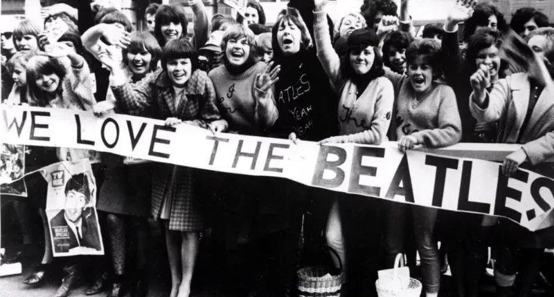 A black and white picture of Beatles fans holding a sign that says