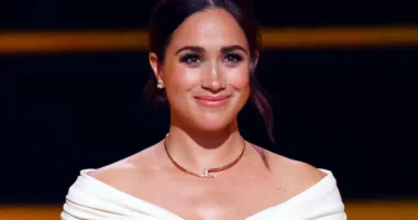 Meghan Markle smiles while wearing a white shoulder skimming top