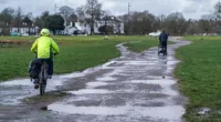 A cyclist riding on Wimbledon Common waterlogged from the rainfall as the met office forecasts unsettled weather conditions over weekend and the threat of more rain
