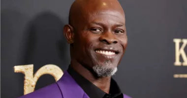 Djimon Hounsou wears a purple jacket and smiles during an event.