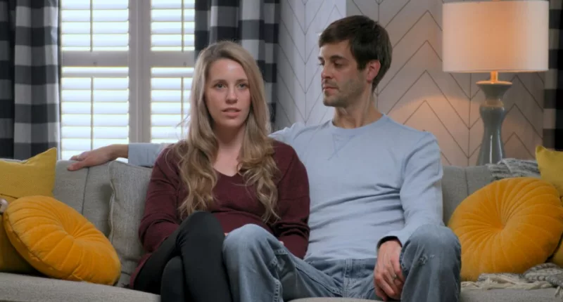 Jill Duggar Dillard and Derick Dillard sitting on a couch in Prime Video docuseries 'Shiny Happy People: Duggar Family Secrets'