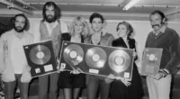 John McVie, Mick Fleetwood, Christine McVie, Lindsey Buckingham, Stevie Nicks, and a friend hold framed records.