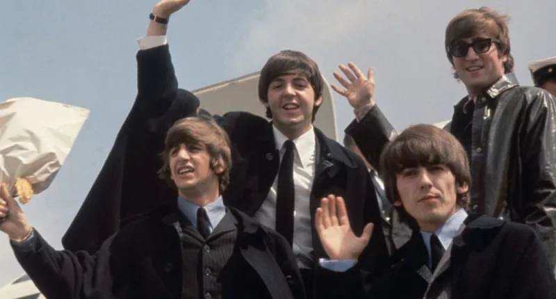 Ringo Starr, Paul McCartney, George Harrison, and John Lennon wave from the entrance to a plane.