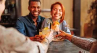 Father's Day - Young African-American man and Hispanic woman toasting cocktail glasses with friends in restaurant.