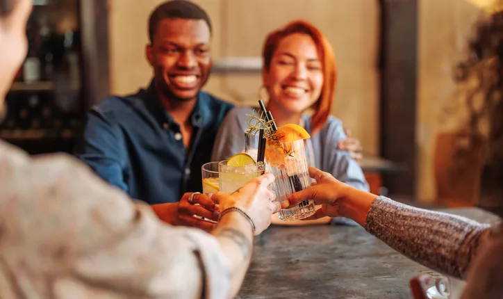 Father's Day - Young African-American man and Hispanic woman toasting cocktail glasses with friends in restaurant.