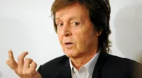 Paul McCartney elevating his right hand while wearing a dark suit during a 2014 event.