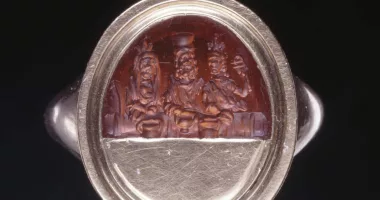 A silver ring with a brown artwork depicting three ancient figures.