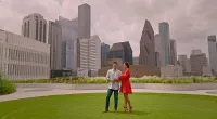 Vanessa and Nick Lachey standing in a park in front of the Houston skyline, where