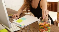 Woman eating candy from glass jar at work