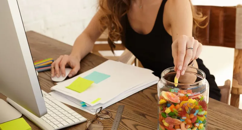 Woman eating candy from glass jar at work