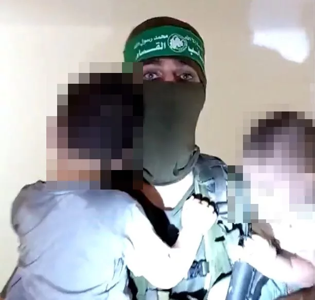 A Hamas fighter holds two Israeli children in his arms