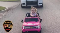 Toddler driving a bright pink toy car is pulled over by cops