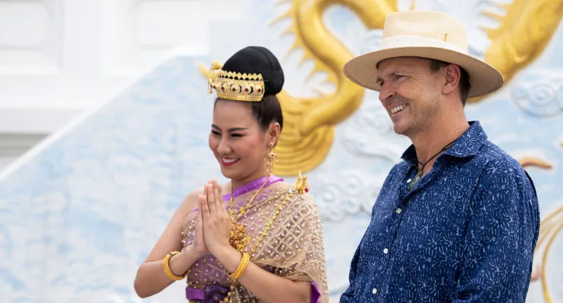 Phil Keoghan standing at the end of the first leg with a woman from Thailand in