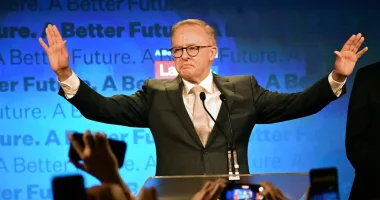 Anthony Albanese raises both hands to the side behind a lectern on election night.