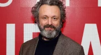Michael Sheen standing in front of a red background