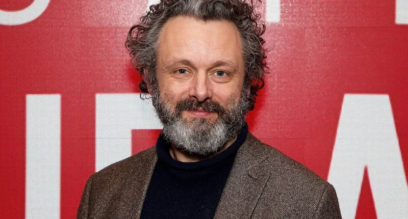 Michael Sheen standing in front of a red background