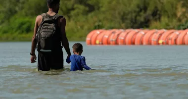 FILE - Migrants walk past large buoys being used as a floating border barrier on the Rio Grande, Aug. 1, 2023, in Eagle Pass, Texas. Texas must move a floating barrier on the Rio Grande that drew backlash from Mexico, a federal appeals court ruled Friday, Dec. 1, 2023, dealing a blow to one of Republican Gov. Greg Abbott