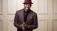 A headshot of Will Packer wearing a purple had and suit