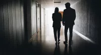 A Business Woman and Business Man walk down a dark hallway together