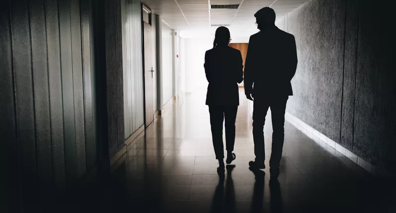 A Business Woman and Business Man walk down a dark hallway together
