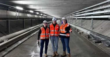 Three women wearing helmets, hi-vis vests and boots standing in a tunnel