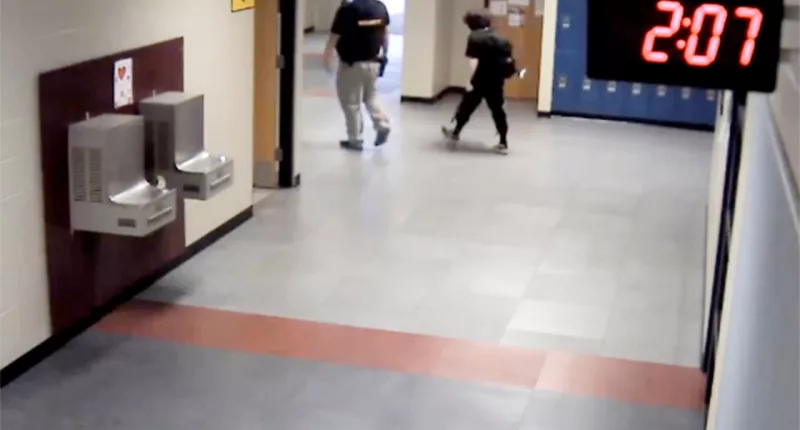 In this image taken from video taken from a school security camera and provided by the Owasso Police Dept., Nex Benedict is seen walking out of the school with a security guard, Feb. 7, 2024, at Owasso High School in Owasso, Okla. A recently released police search warrant is revealing more details in the case of a Benedict, a nonbinary student, who died a day after a high school bathroom fight. (School Security Video/Courtesy of Owasso Police Department via AP)