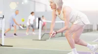 mature woman with gray hair in tennis dress playing tennis in indoor court