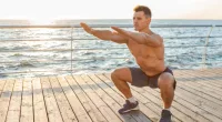 fit man doing squats on boardwalk by the ocean at sunrise or sunset