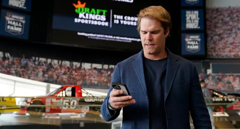 FILE - Fox Sports broadcaster Greg Olsen retrieves his receipt after placing the first ceremonial bet in North Carolina during a DraftKings event celebrating the launch of mobile and online sports wagering across the state at the NASCAR Hall of Fame, Monday, March 11, 2024, in Charlotte, N.C. As March Madness gets underway, more people than ever now can legally bet on sports. A total of 38 states and the District of Columbia now allow some form of sports betting.(AP Photo/Erik Verduzco, File)