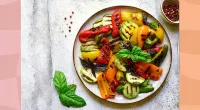 colorful roasted vegetables on a plate with small bowl of pepper on the side
