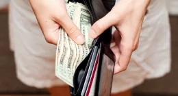 a person holding a wallet with U.S dollars