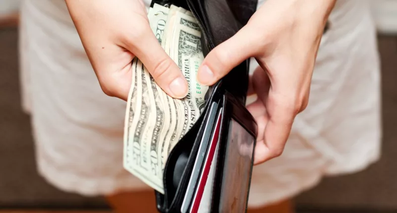 a person holding a wallet with U.S dollars