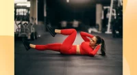 fit woman in red athletic attire doing bicycle crunches at the gym