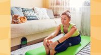 woman doing forward fold stretch on green yoga mat in bright living space