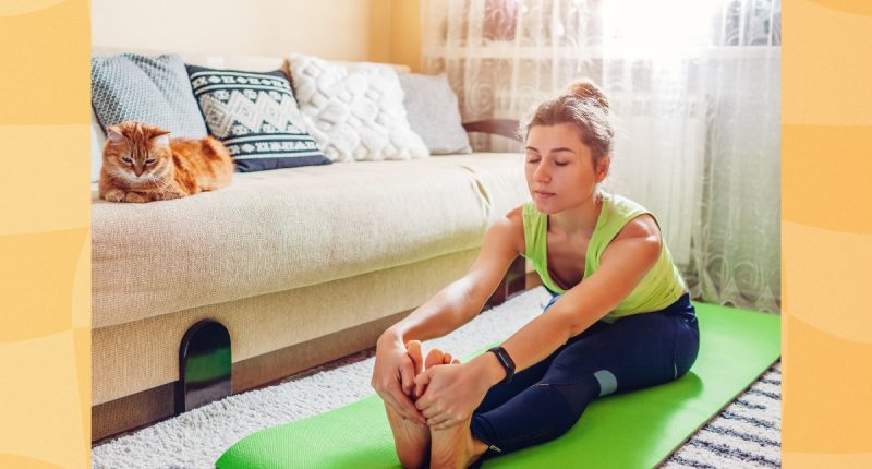 woman doing forward fold stretch on green yoga mat in bright living space