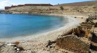 A view of the abandoned prison on Gyaros island with crystal-clear blue waters and a white pebble beach