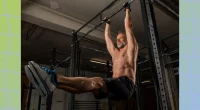 muscular, middle-aged shirtless man doing pull-up exercises in dark gym weight room