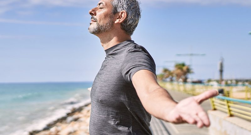 Middle age hispanic man wearing sportswear breathing at seaside