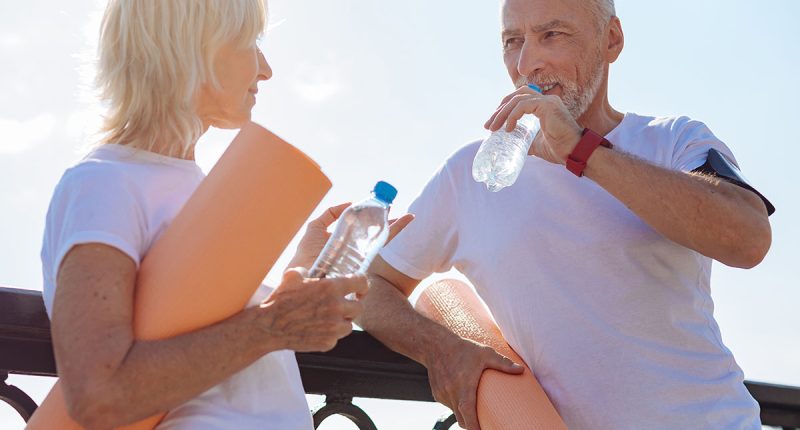 lderly couple discussing their yoga practice, drinking from water bottles