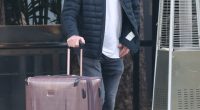 Dennis Quaid pulling a suitcase outside a hotel.