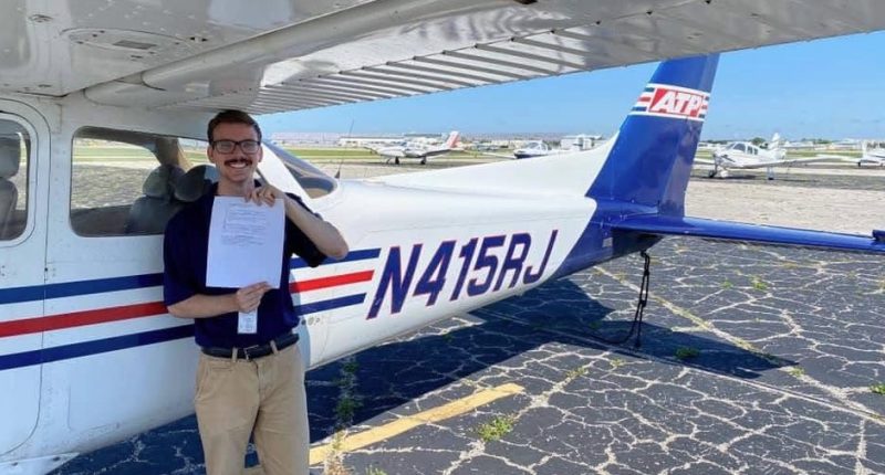 Pilot holding his certificate in front of a small airplane.