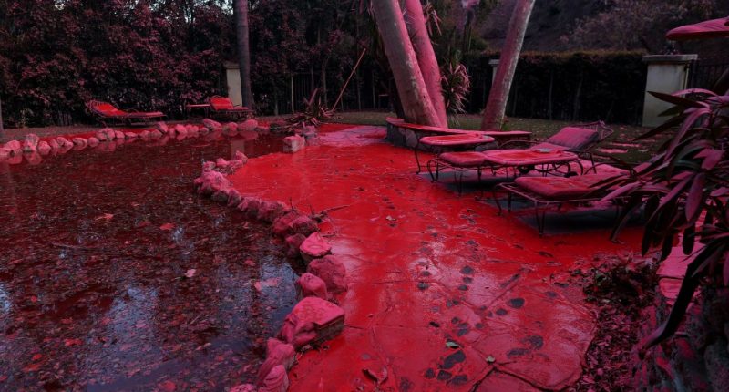 Fire retardant covers a pool and lounge chairs after being dropped from a firefighting aircraft battling the Palisades Fire