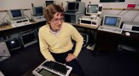 Bill Gates sitting at a desk among many computers.