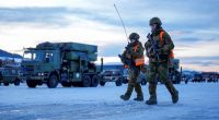 Two soldiers carrying rifles walk in the snow.