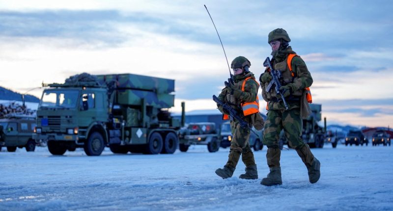 Two soldiers carrying rifles walk in the snow.