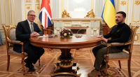 Two men sitting at a table, one with the UK flag behind him and the other with the Ukrainian flag.