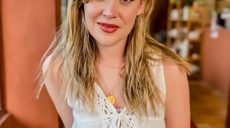 Woman with long blonde hair wearing a white crocheted top.