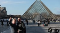 Couple taking a selfie in front of the Louvre Pyramid in Paris.